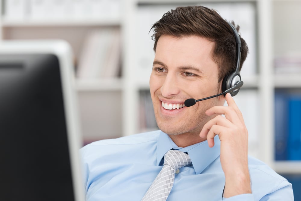 Smiling friendly handsome young male call centre operator or client services personnel beaming as he listens to a call and checks information on his computer monitor-Sep-26-2023-04-57-22-9729-PM